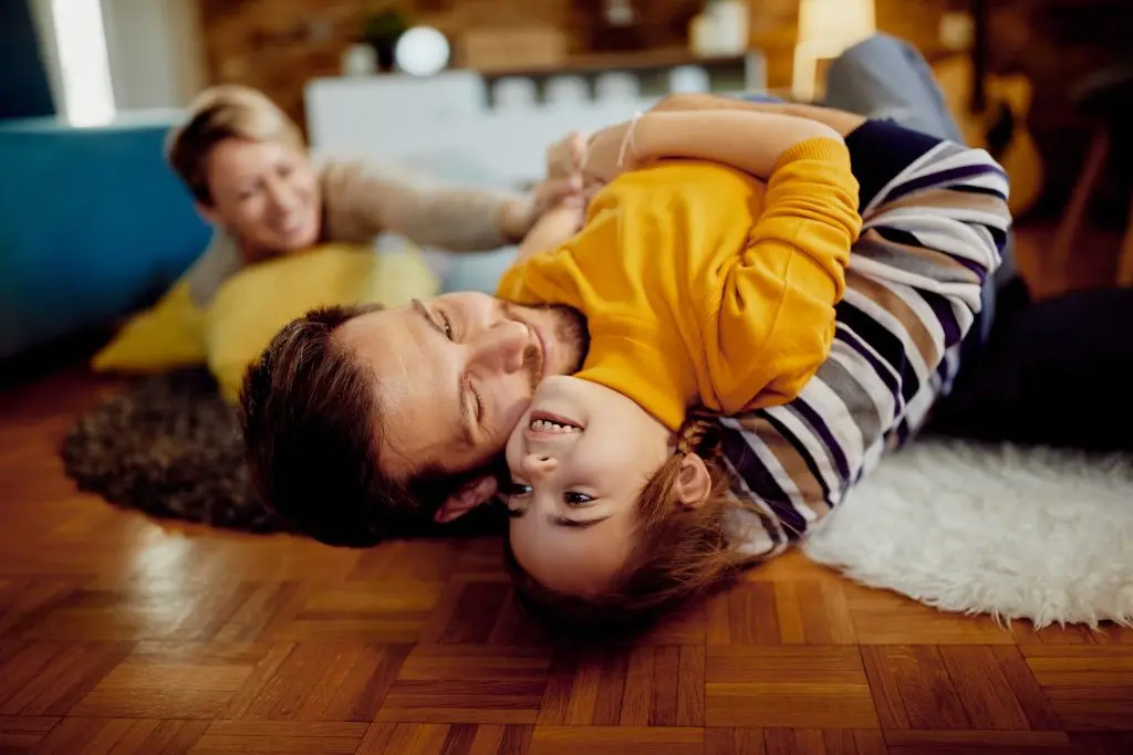Un père et sa fille sont allongés sur un plancher de bois. Ils sont en train de jouer ensemble.