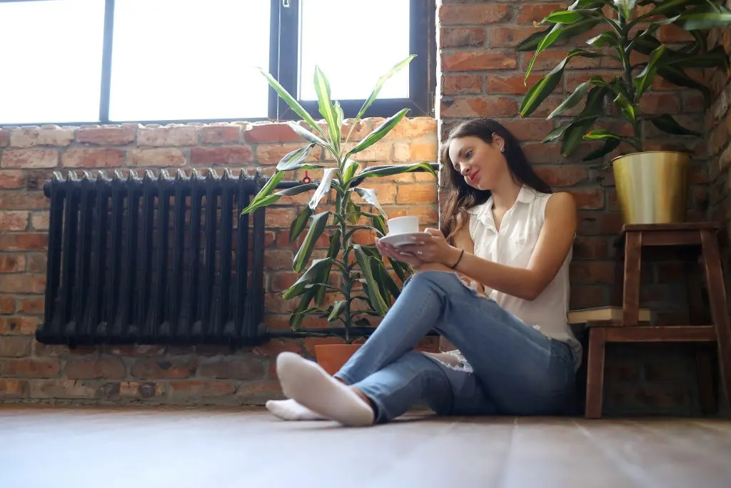 Une femme assise sur le sol. Bois un thé proche d'un radiateur couleur noir.